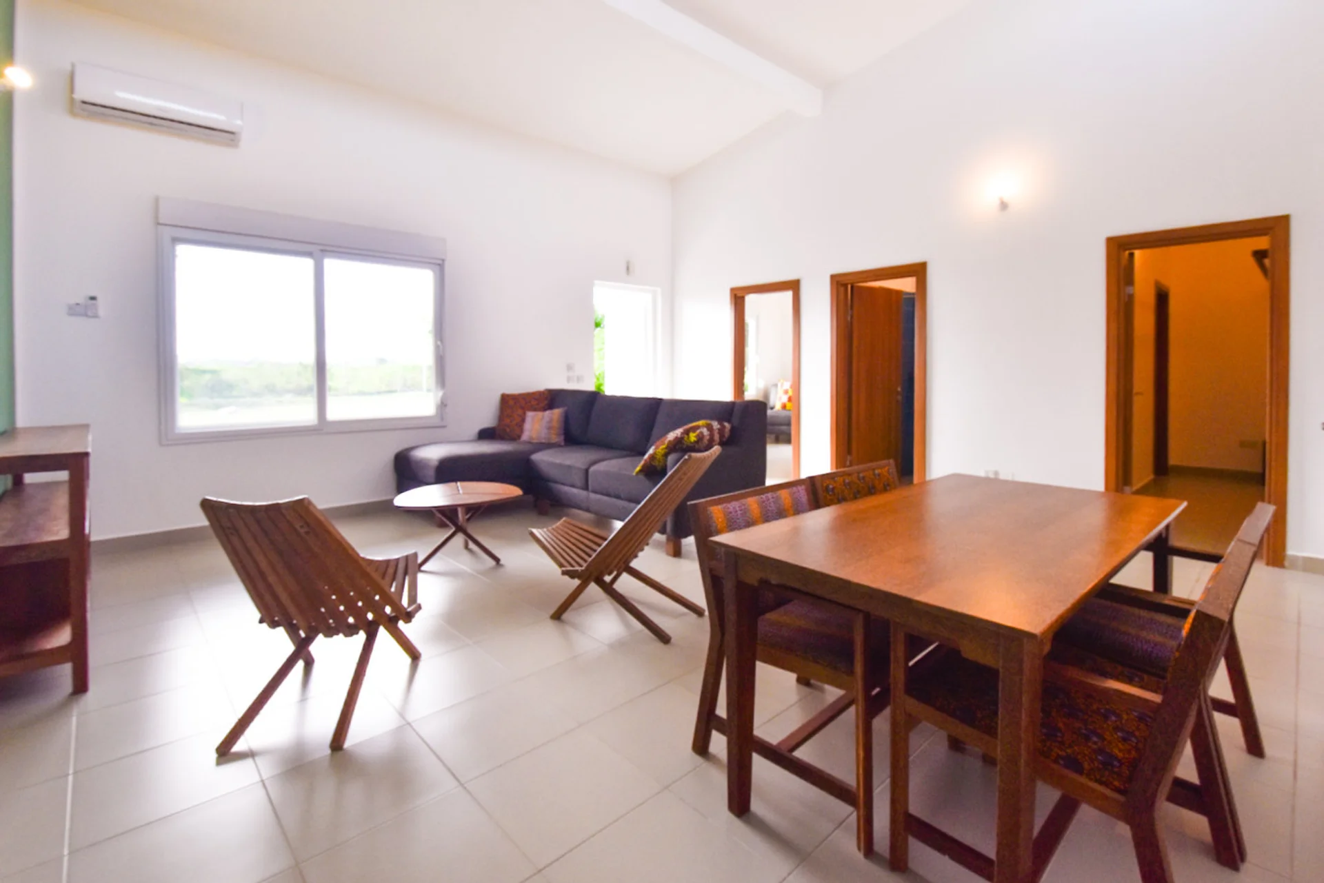 Bright living and dining room with a grey corner sofa, timber furniture and large windows.