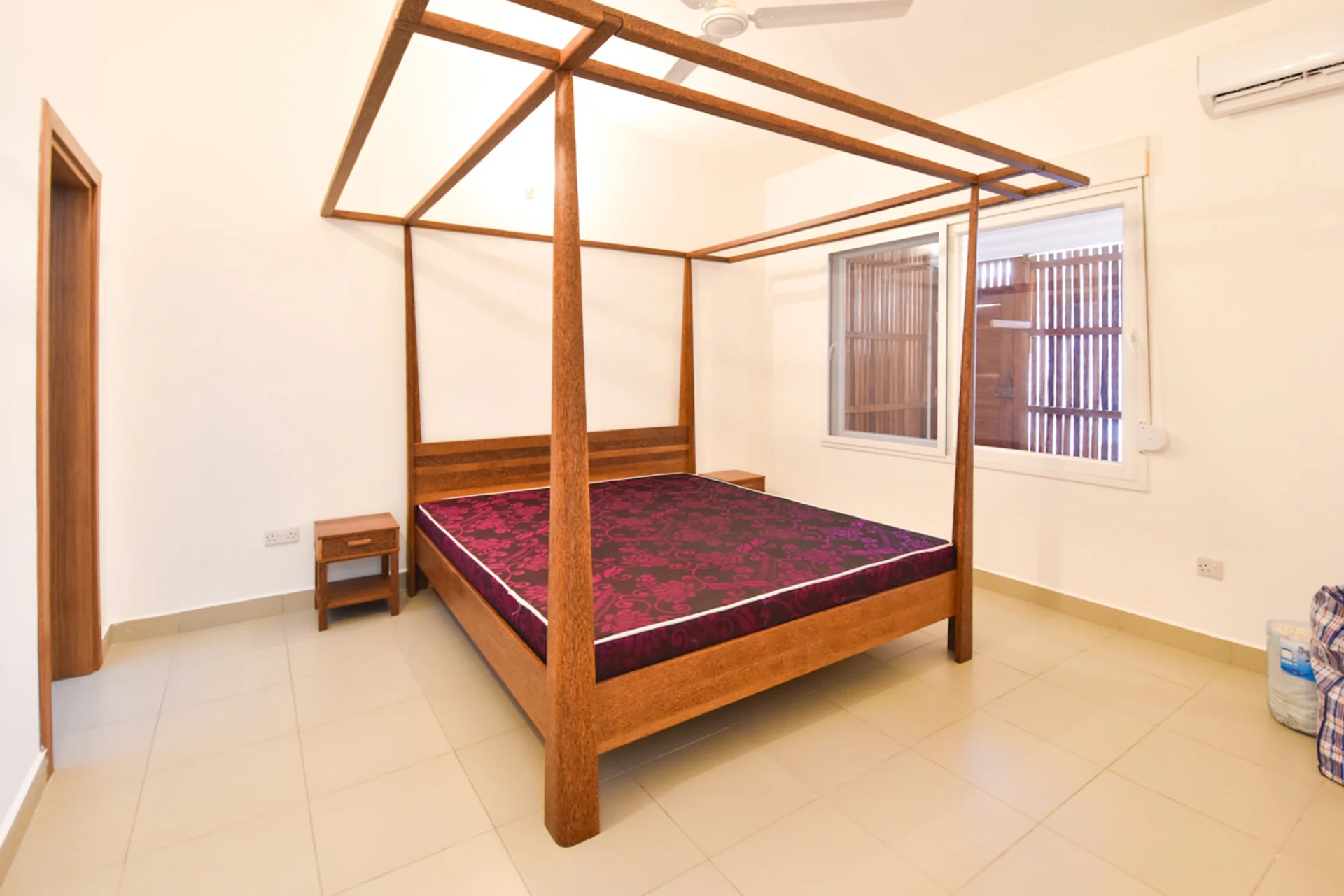 Bedroom with a timber four-poster bed, red mattress, ceiling fan and air conditioning.