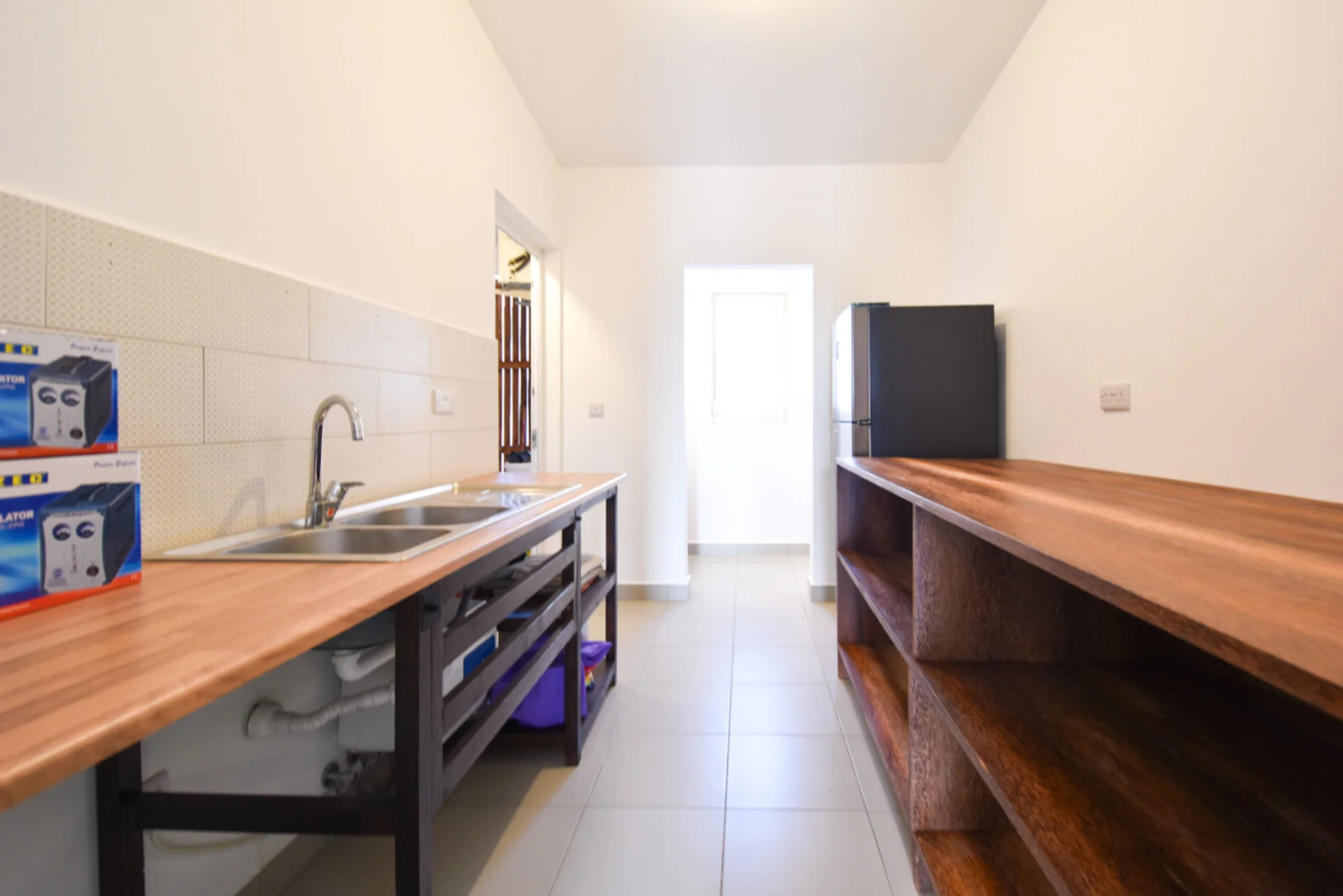 Galley kitchen with timber worktops, double sink, open shelving and refrigerator.