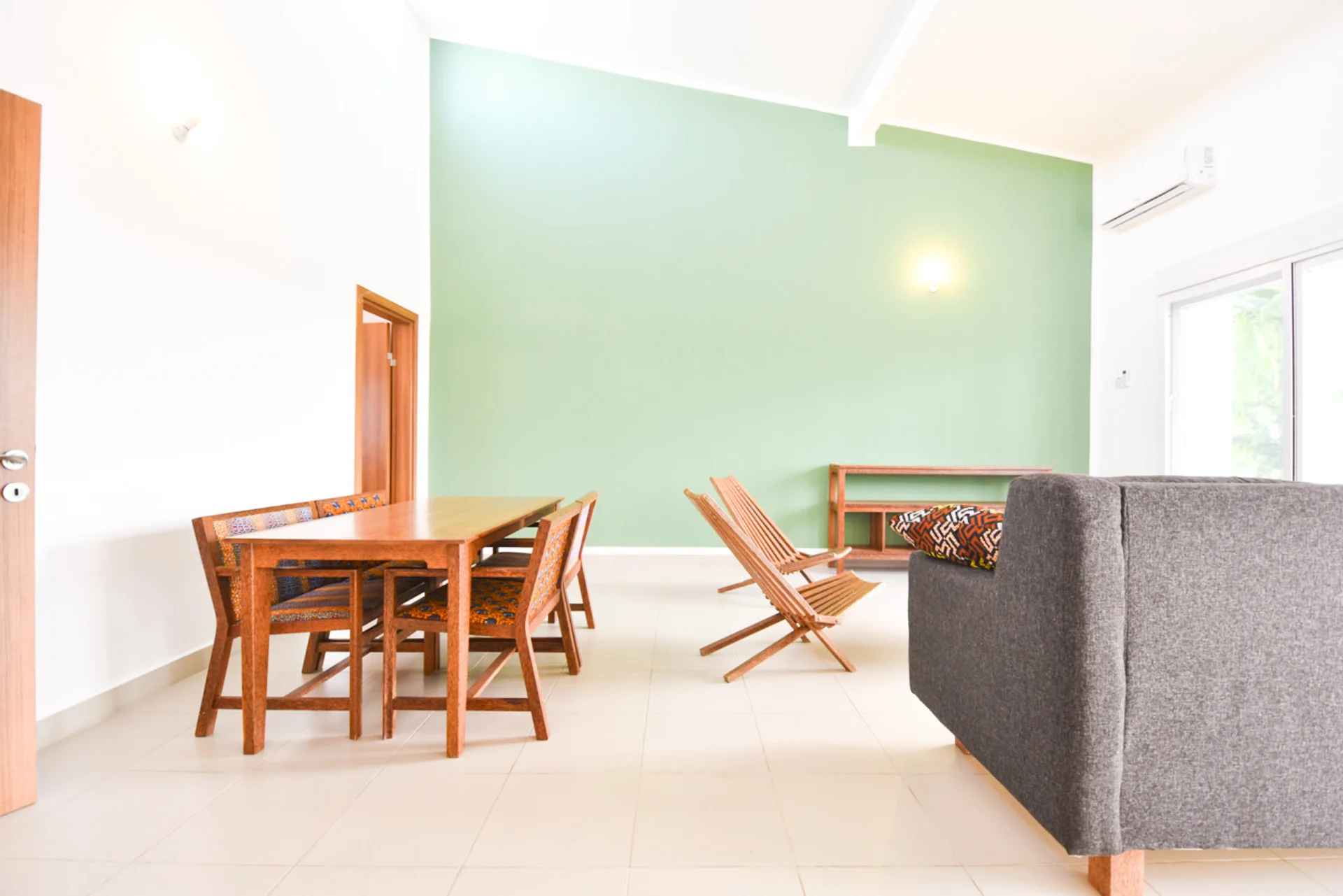 View past the grey sofa toward the green feature wall and timber dining furniture.