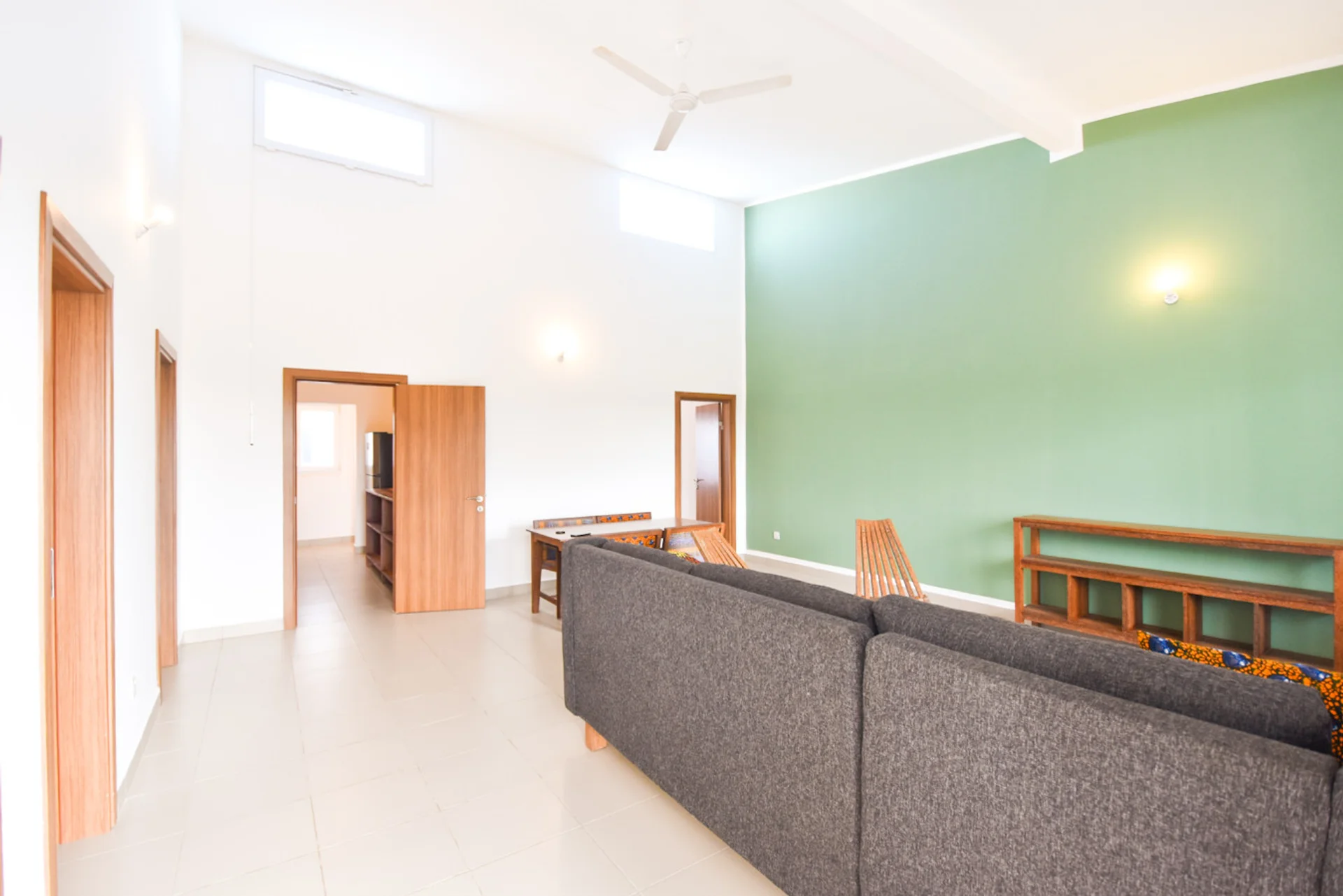 Open living area with a green wall, high windows and ceiling fan.