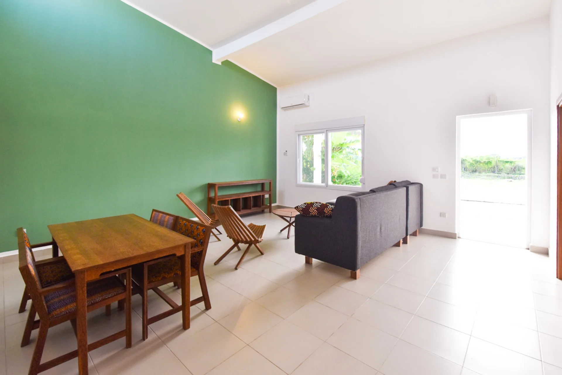 Dining table beside the green feature wall, with the lounge and garden door beyond.