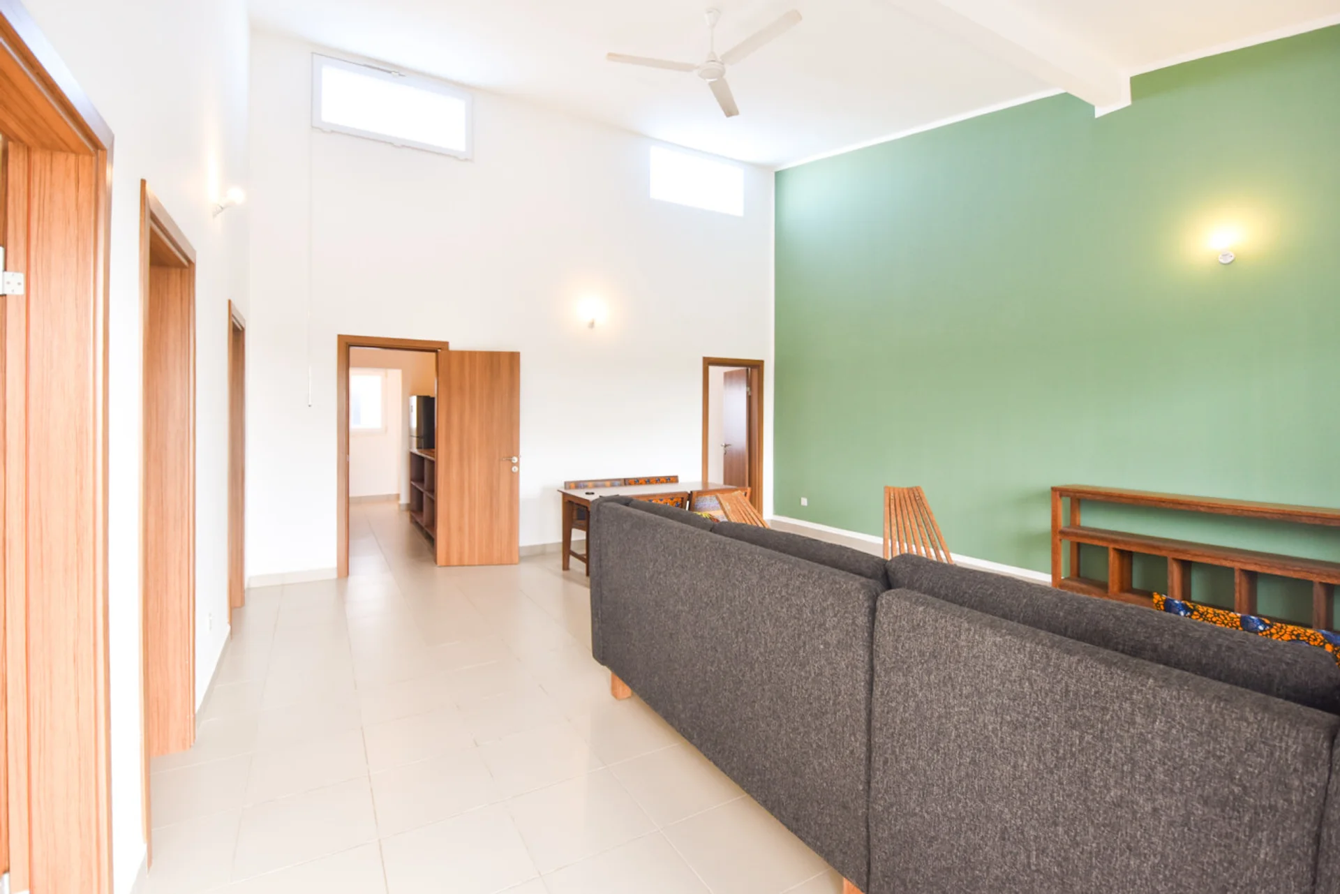 View across the grey corner sofa toward the hallway and green feature wall.