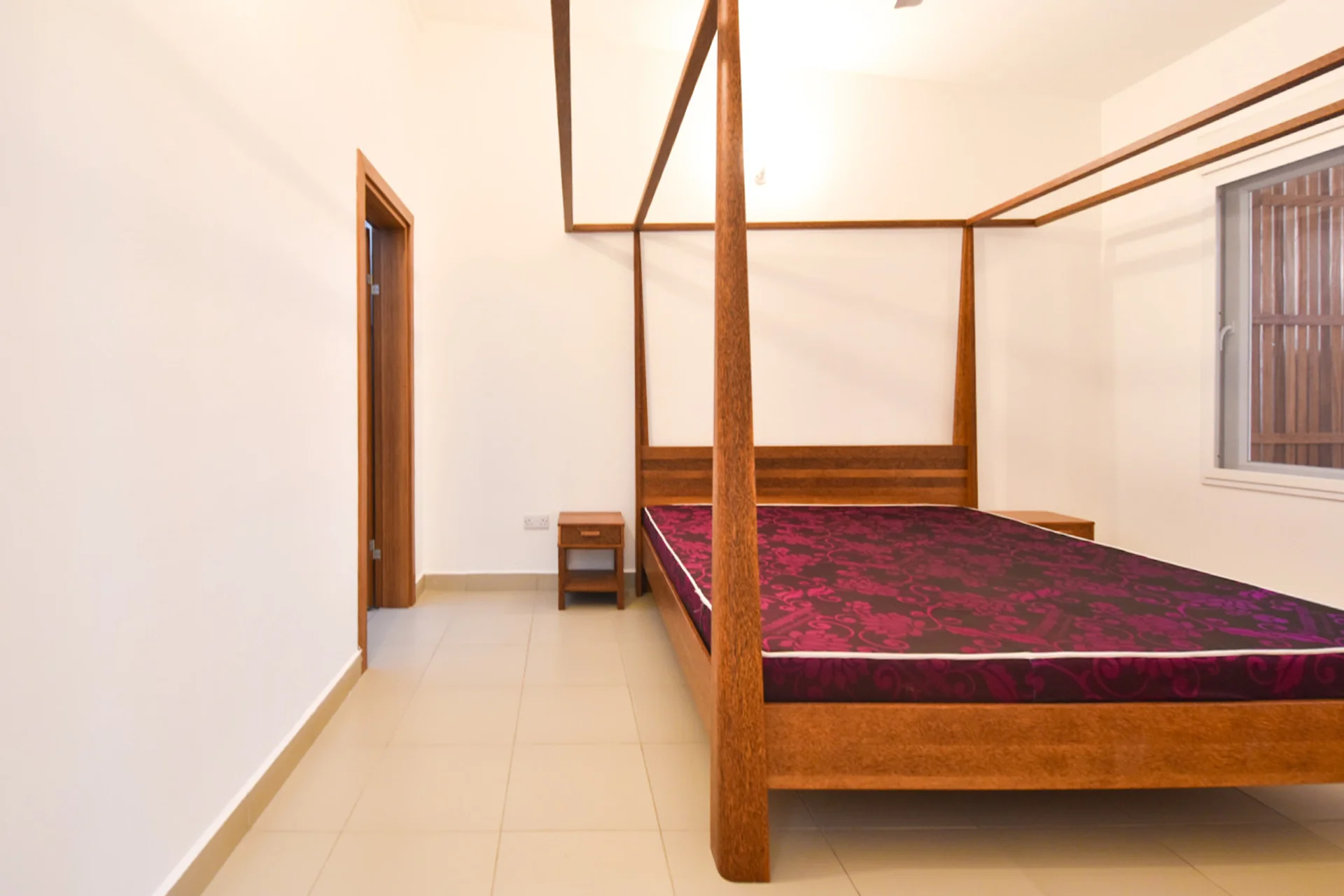 Timber four-poster bed with a red mattress beside the bedroom doorway.