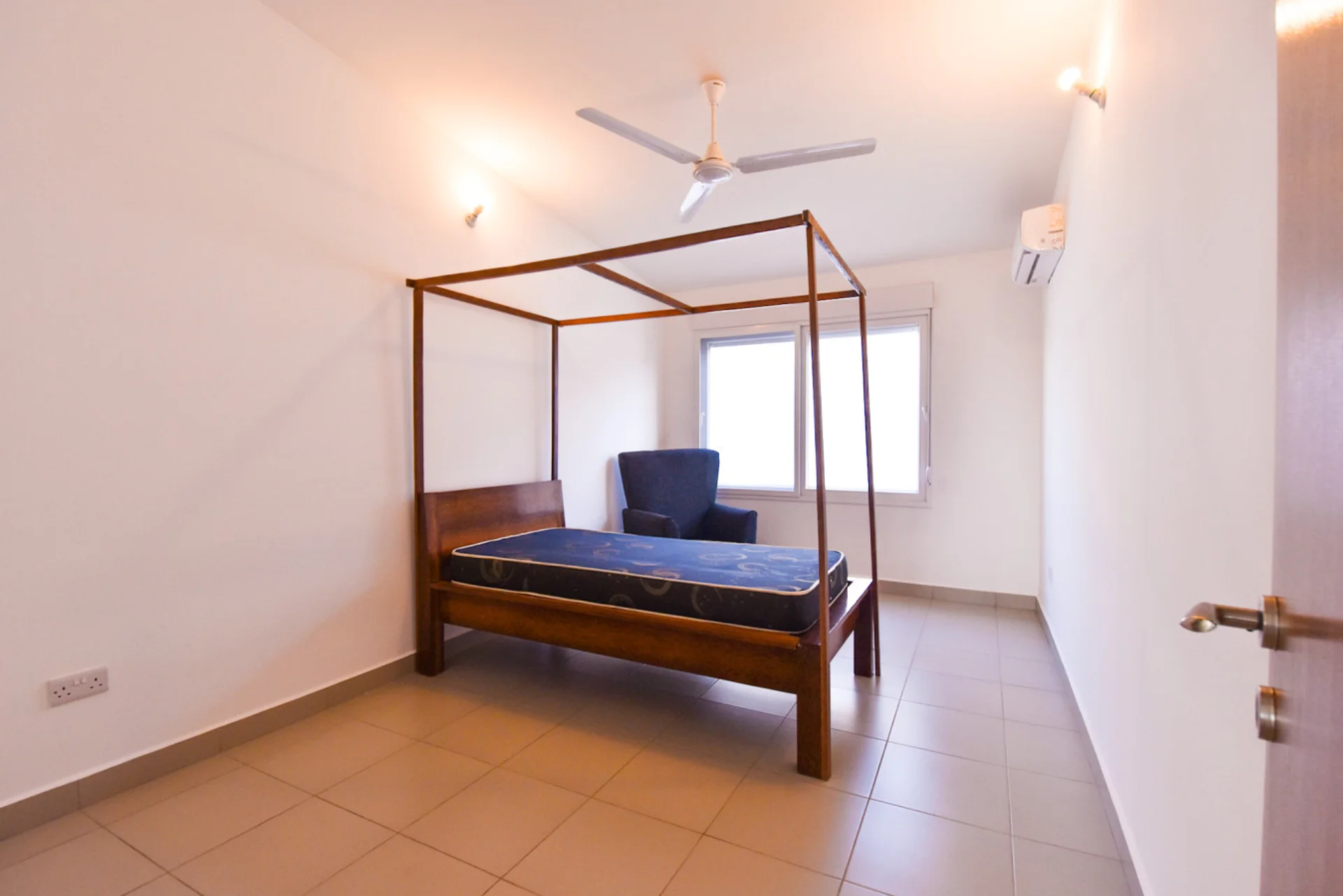 Blue-mattress four-poster bed in a bright room with a ceiling fan.