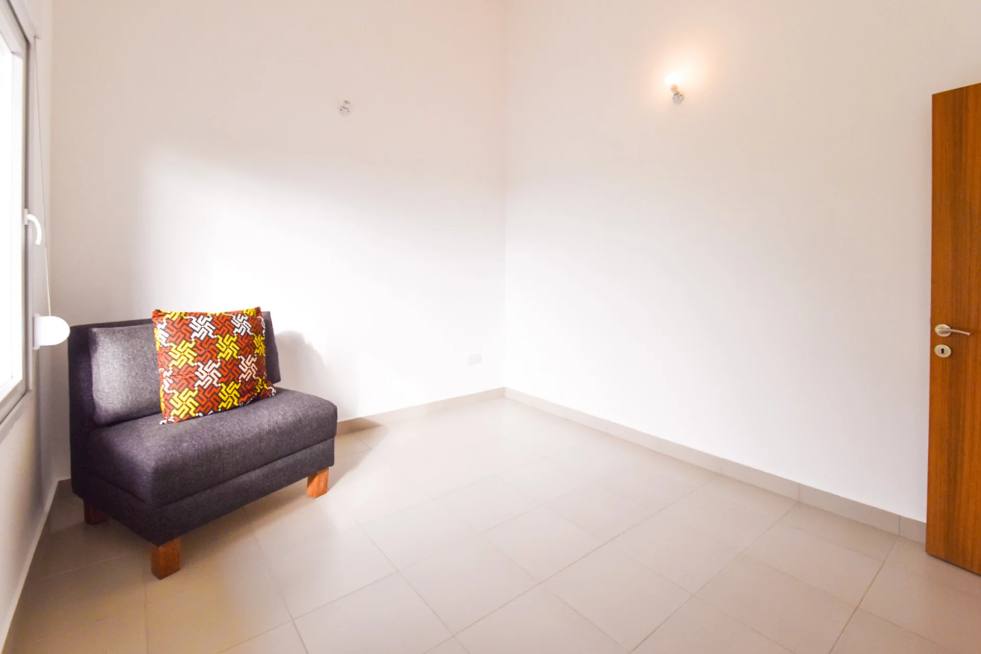 Uncluttered spare room with a dark upholstered chair and tiled floor.