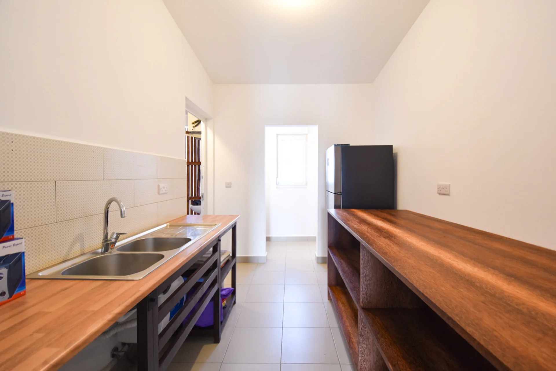 Kitchen passage with double sink, open timber shelves and refrigerator.