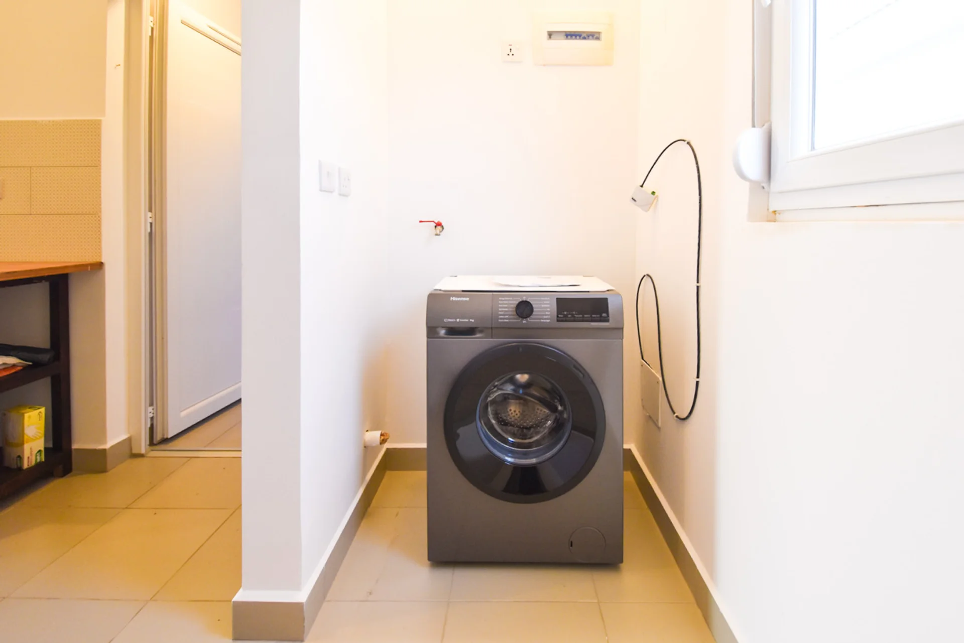 Front-loading washing machine in a tiled laundry nook beneath a window.
