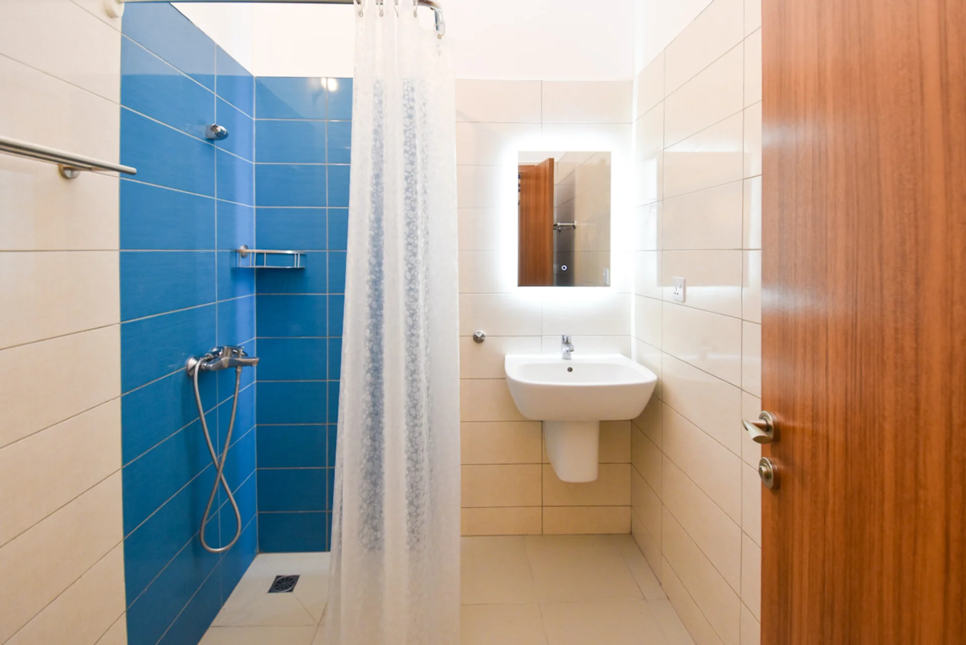 Shower room with a blue tiled shower wall, basin and illuminated mirror.