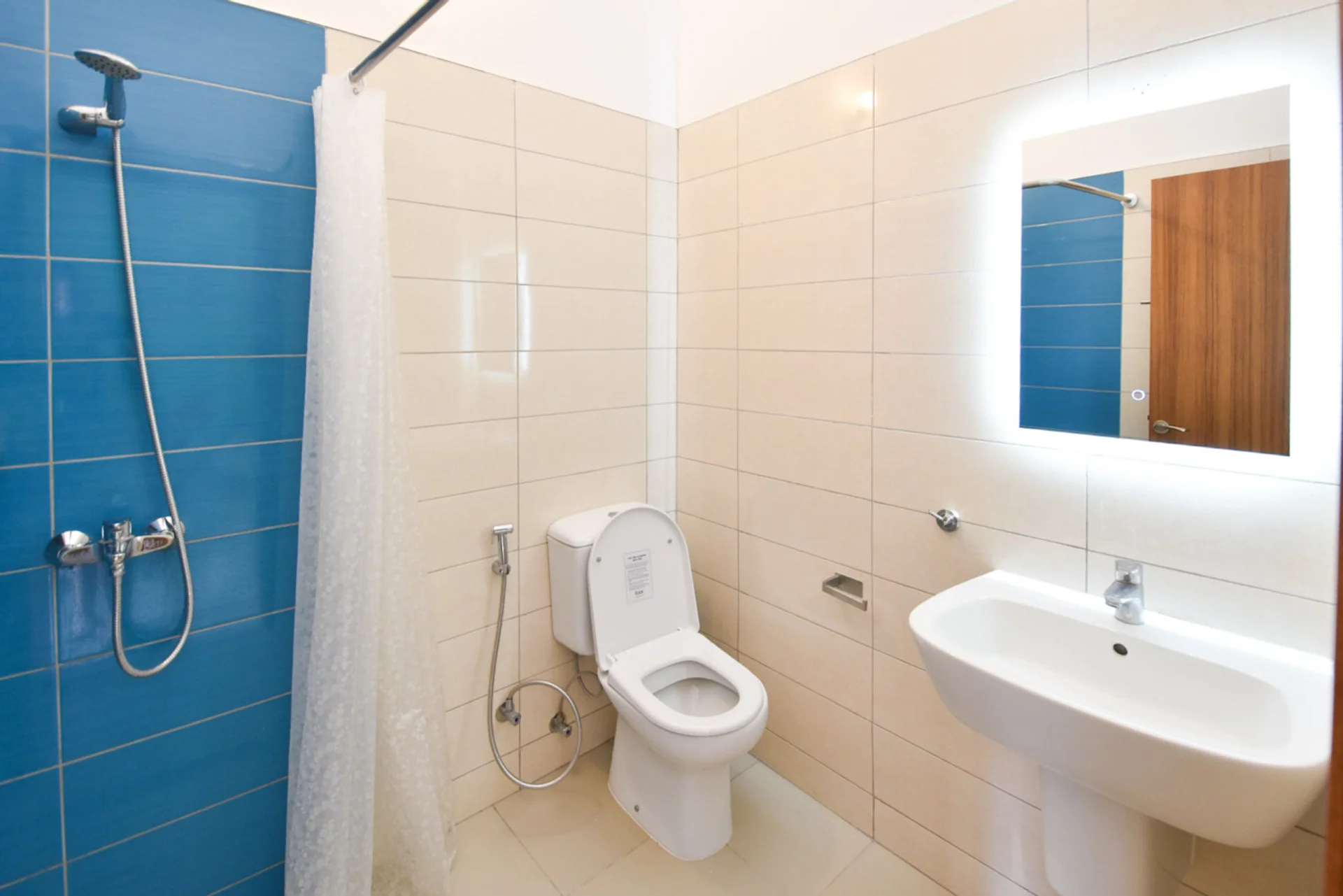 Bathroom with a blue tiled shower area, toilet, white basin and mirror.