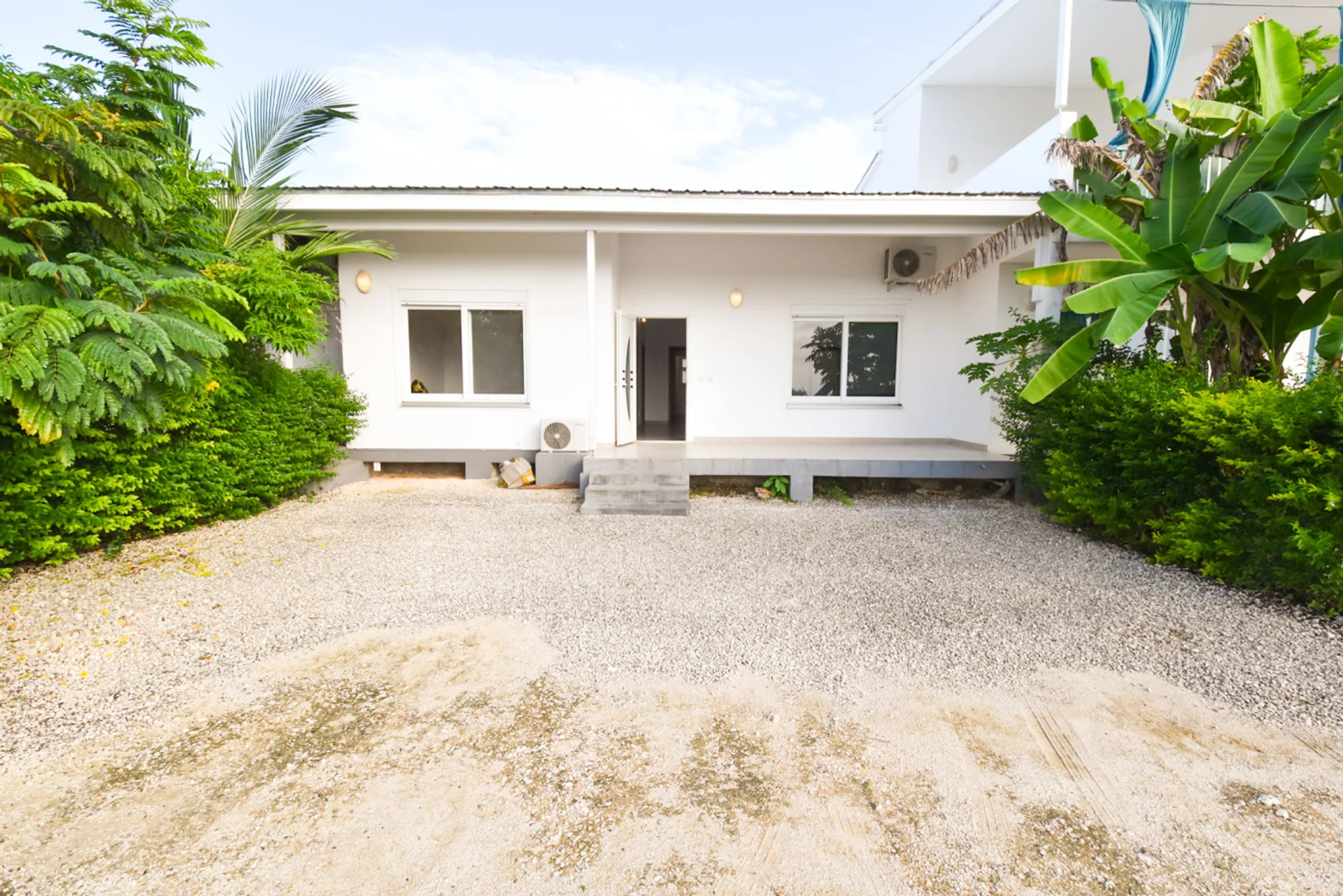 Front view of the white townhouse and gravel courtyard surrounded by tropical plants.